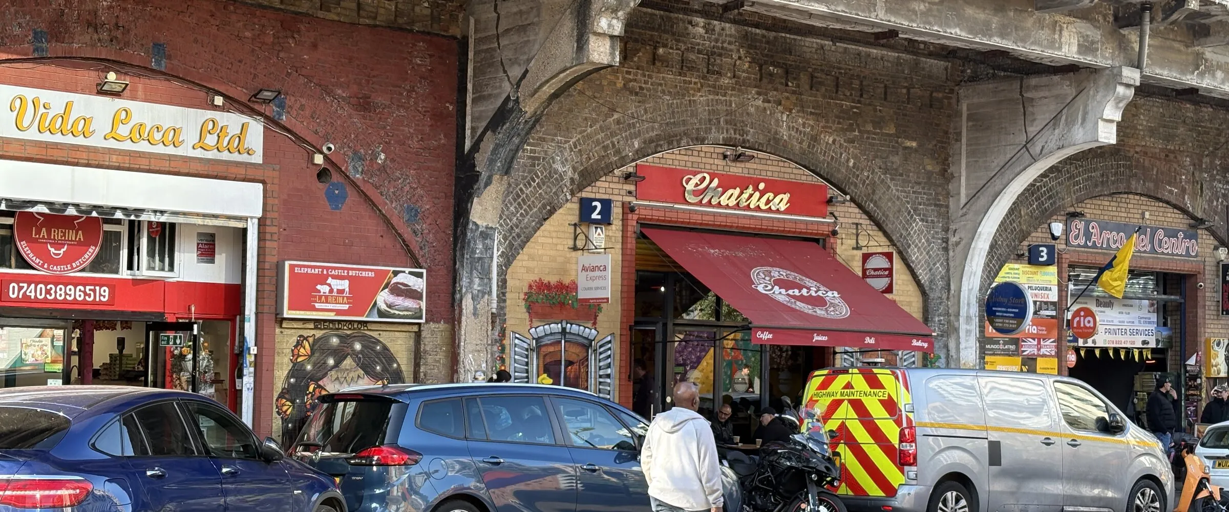 Latin American businesses trading from the brick railway arches on Elephant Road, with new residential towers behind.