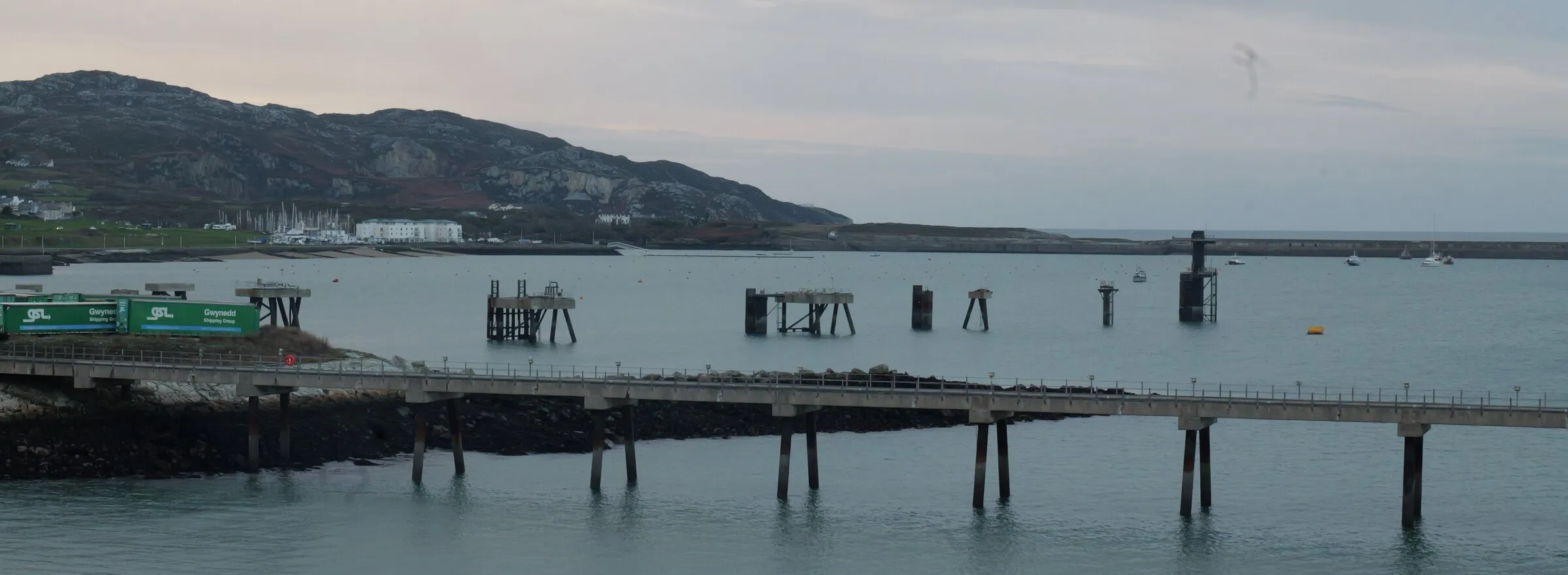 The breakwater and timber jetty at Holyhead at dusk, with the headland behind.