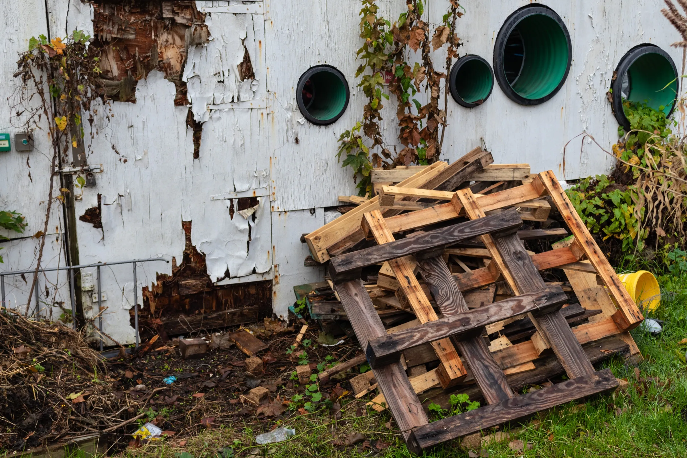 Salvaged pallets and timber stacked against a weathered white wall at the Story Garden.